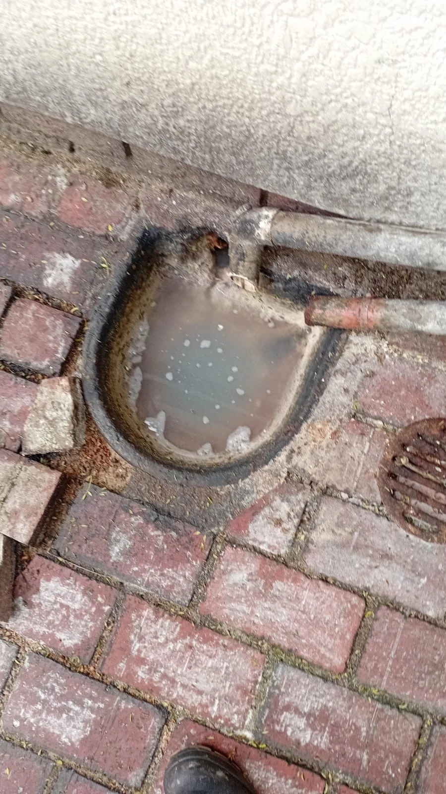 Outside gully overflowing with dirty standing water beside paving.