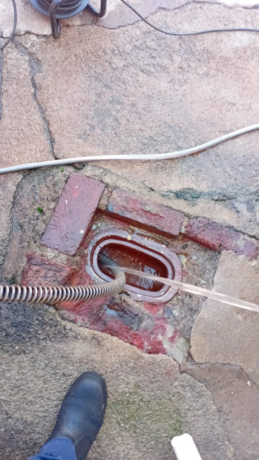 Drain cleaning cable clearing a main outside drain through an inspection opening.